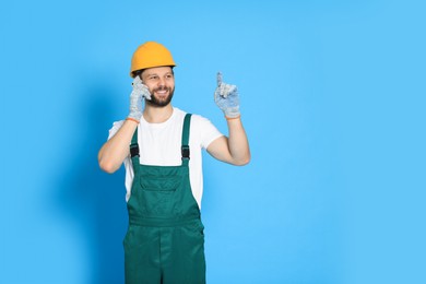 Photo of Professional repairman in uniform talking on smartphone against light blue background. Space for text