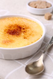 Photo of Delicious creme brulee in bowl and spoon on table, closeup