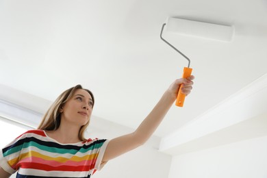 Young woman painting ceiling with white dye indoors