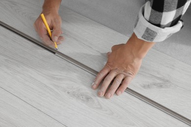 Photo of Professional worker using pencil during installation of new laminate flooring, closeup