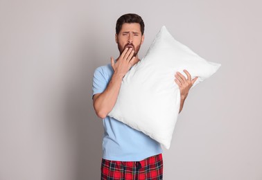 Photo of Tired man with pillow yawns on light grey background