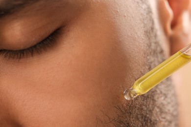 Man applying cosmetic serum onto face, closeup