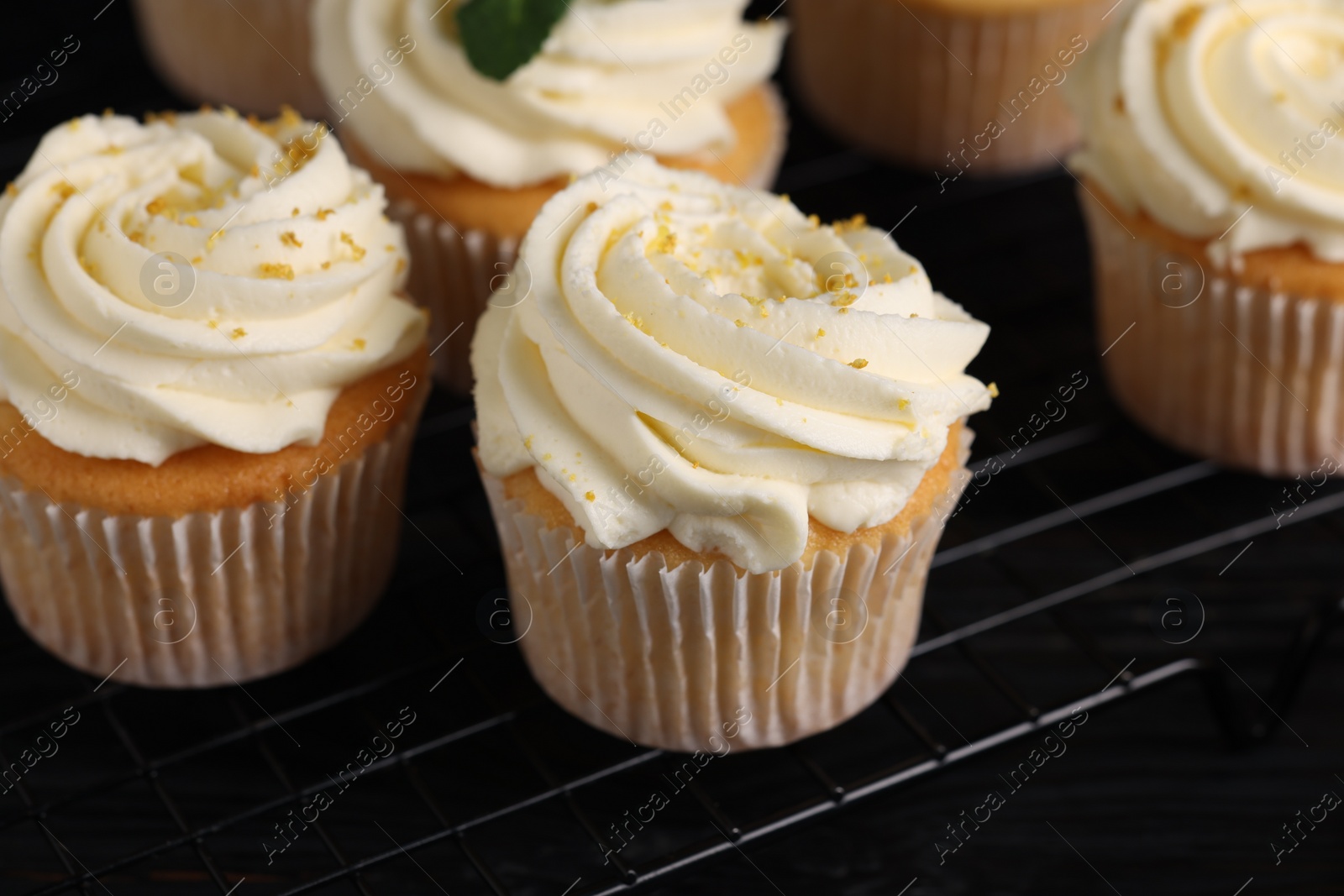Photo of Delicious cupcakes with white cream and lemon zest on cooling rack, closeup