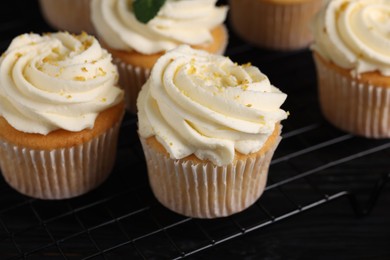 Delicious cupcakes with white cream and lemon zest on cooling rack, closeup