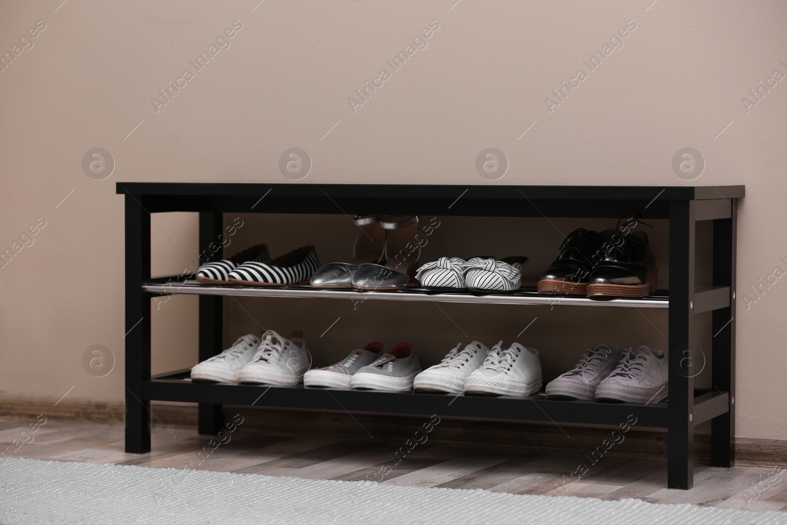 Photo of Shoe rack with different footwear near color wall. Stylish hallway interior