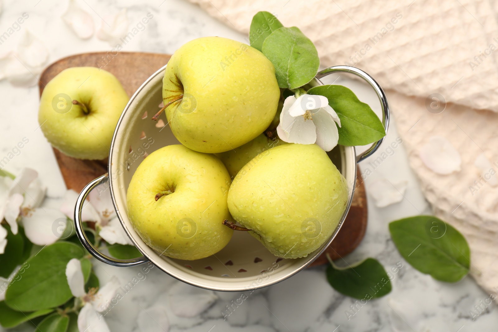 Photo of Colander with fresh apples and beautiful spring blossoms on white marble table, flat lay