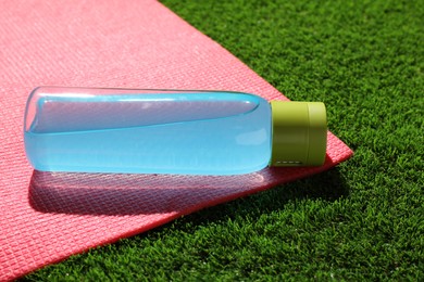 Photo of Bottle of light blue drink and mat on green grass