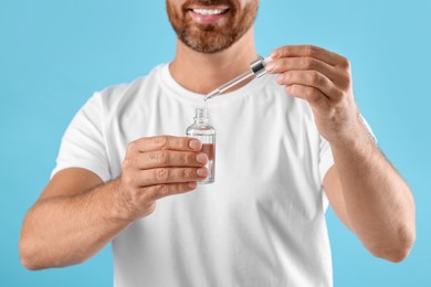 Smiling man with cosmetic serum on light blue background, selective focus