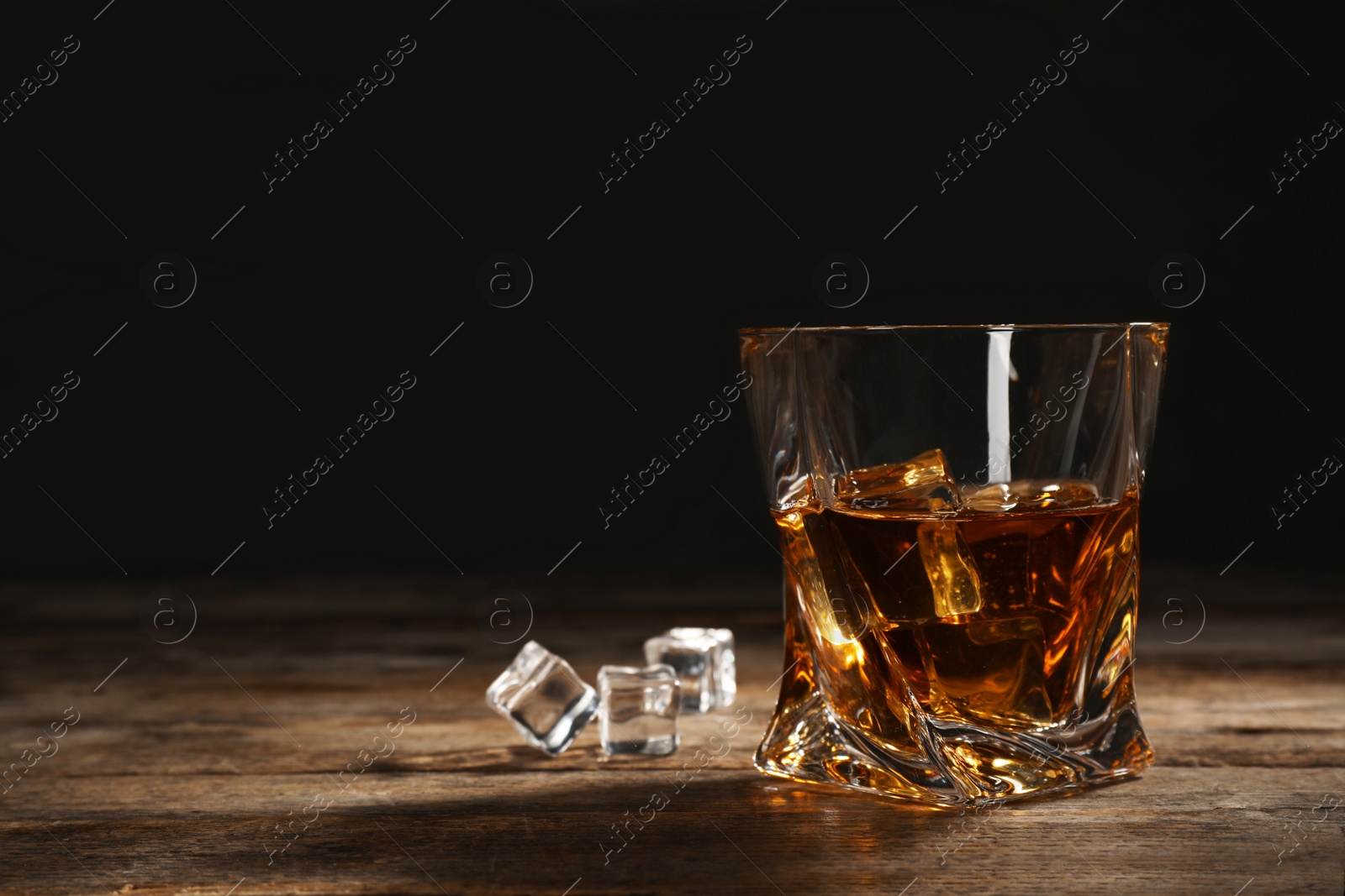 Photo of Golden whiskey in glass with ice cubes on table. Space for text