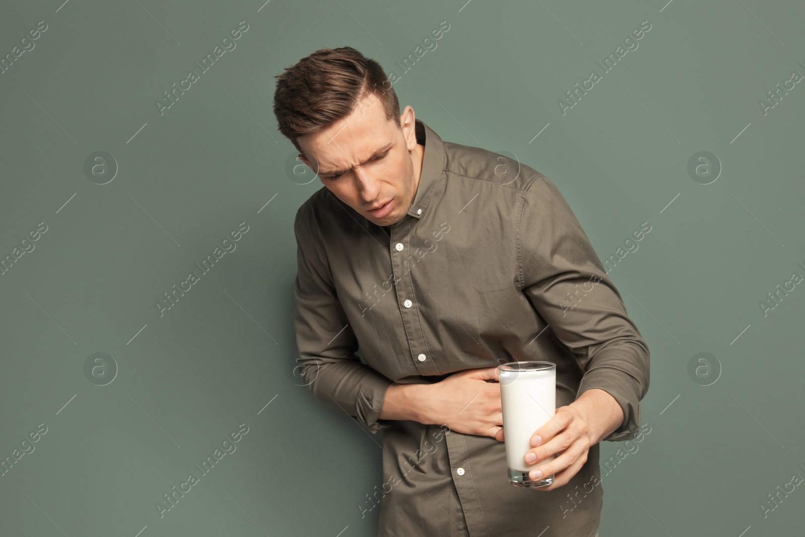 Photo of Young man with dairy allergy holding glass of milk on color background