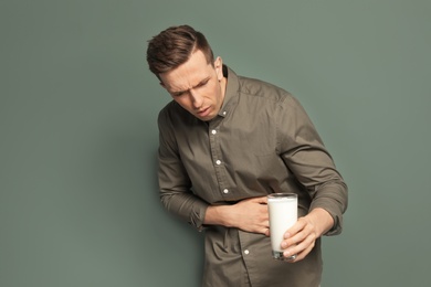 Young man with dairy allergy holding glass of milk on color background
