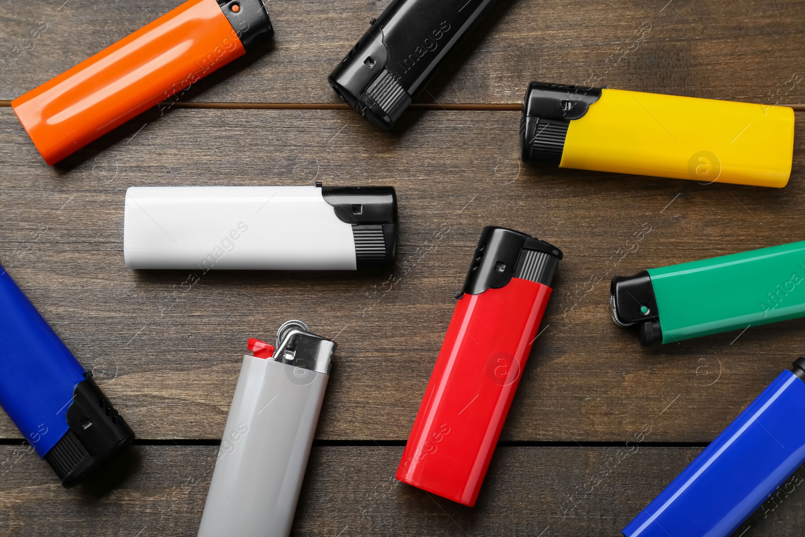 Photo of Colorful plastic cigarette lighters on wooden table, flat lay