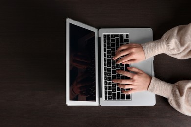 Woman working with laptop at wooden table, top view. Space for text