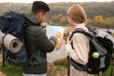 Couple of travelers with backpacks and map planning trip in mountains, back view. Autumn vacation