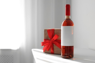 Photo of Bottle of wine and gift box on table in light room. Space for text