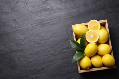 Many fresh ripe lemons with green leaves on black table, top view. Space for text