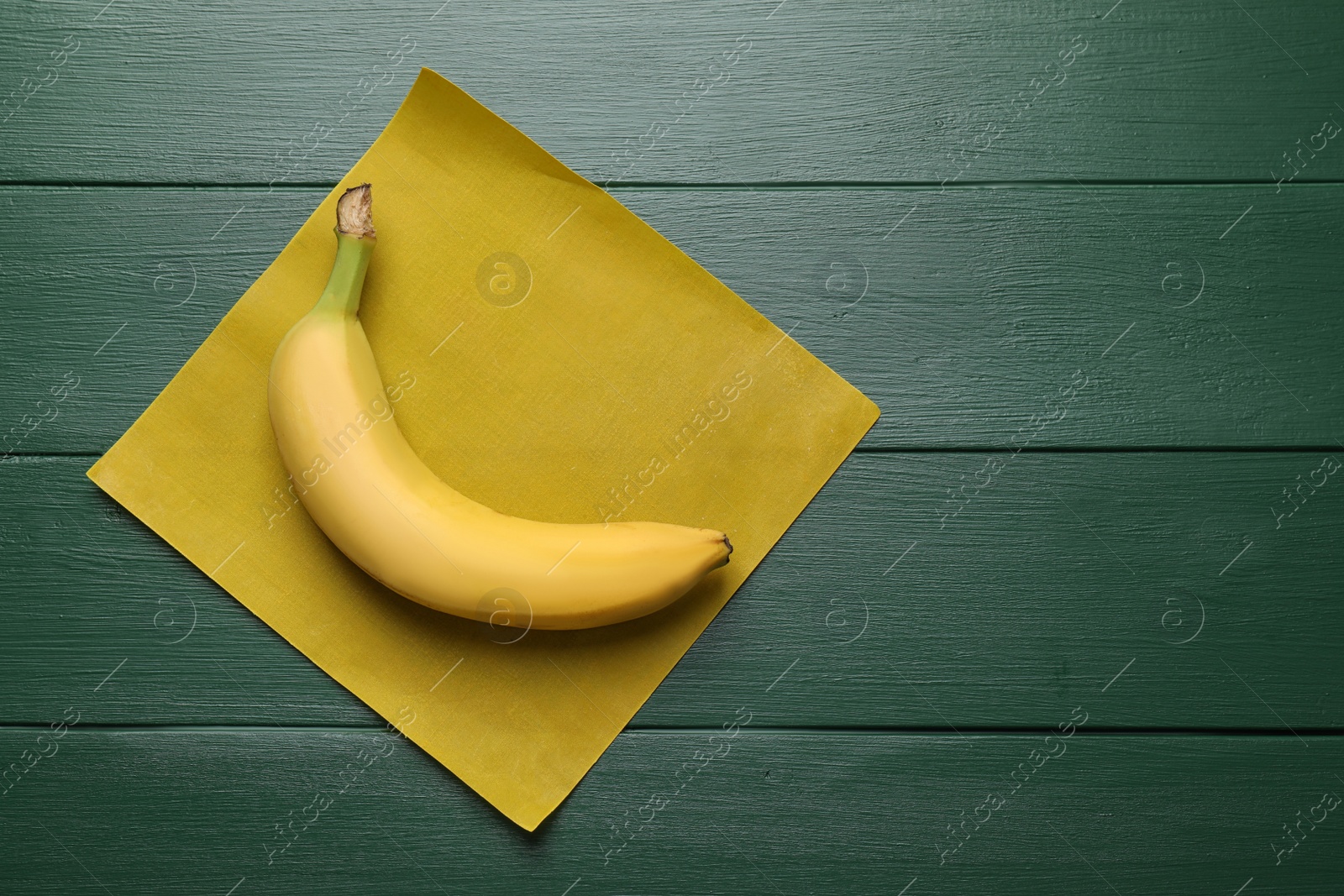 Photo of Fresh ripe banana and waxed napkin on green wooden table, top view. Space for text