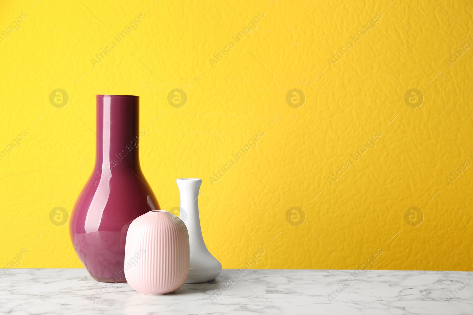 Photo of Stylish ceramic vases on white marble table against yellow background. Space for text