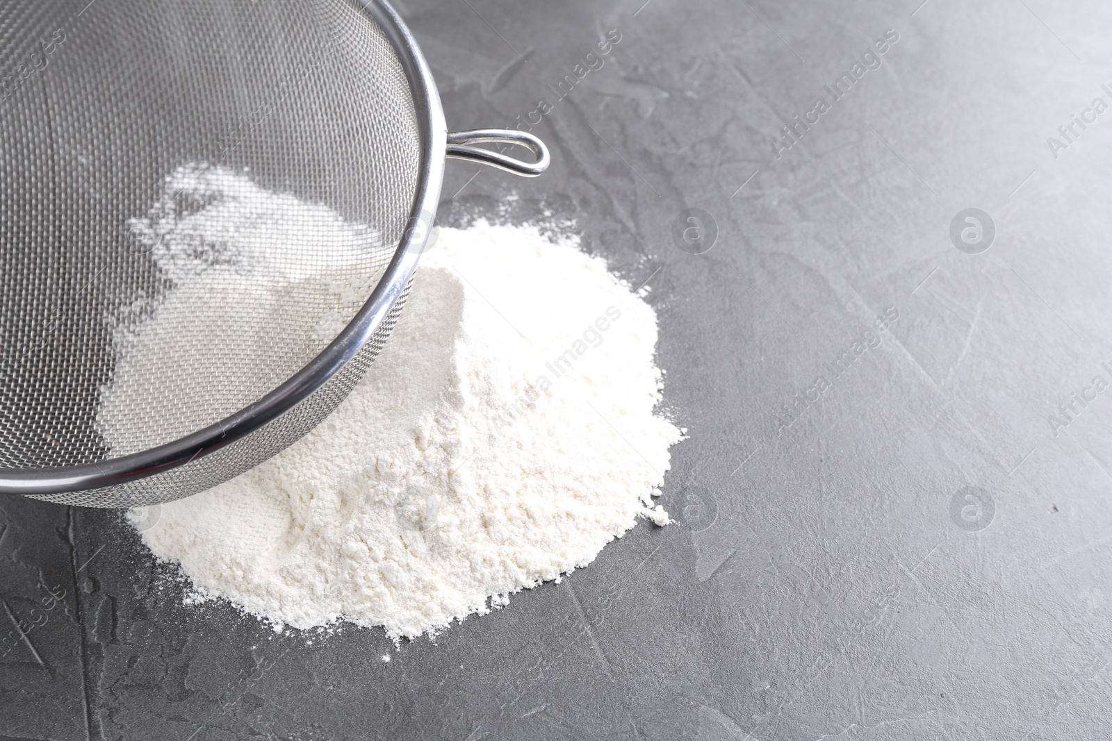 Photo of Metal sieve and flour on grey table. Space for text