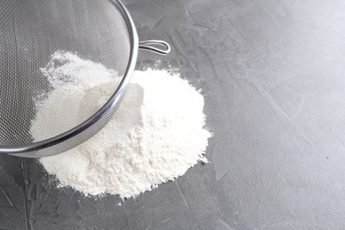 Metal sieve and flour on grey table. Space for text