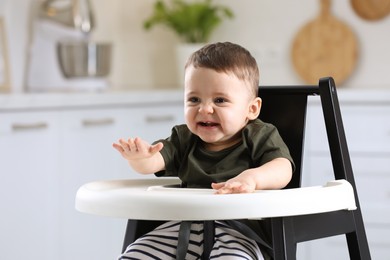 Photo of Cute little baby sitting in high chair at kitchen