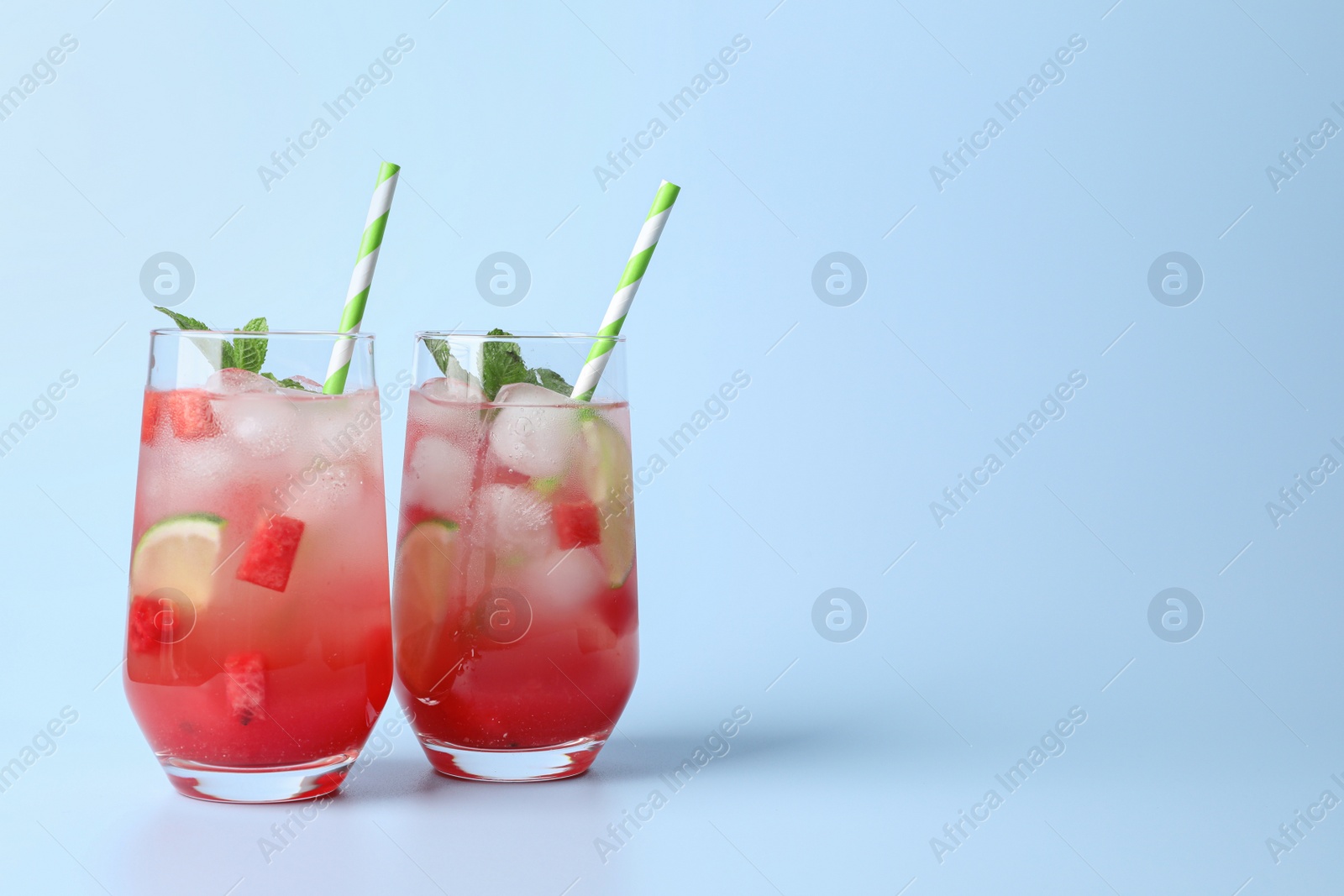 Photo of Tasty summer watermelon drink with lime in glasses on pale light blue background. Space for text