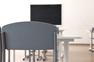 Photo of Empty school classroom with desks, blackboard and chairs