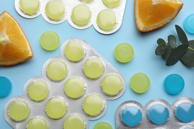 Many cough drops, eucalyptus and slices of orange on light blue background, flat lay