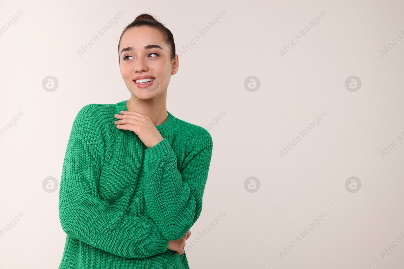 Photo of Beautiful young woman in stylish warm sweater on light grey background, space for text