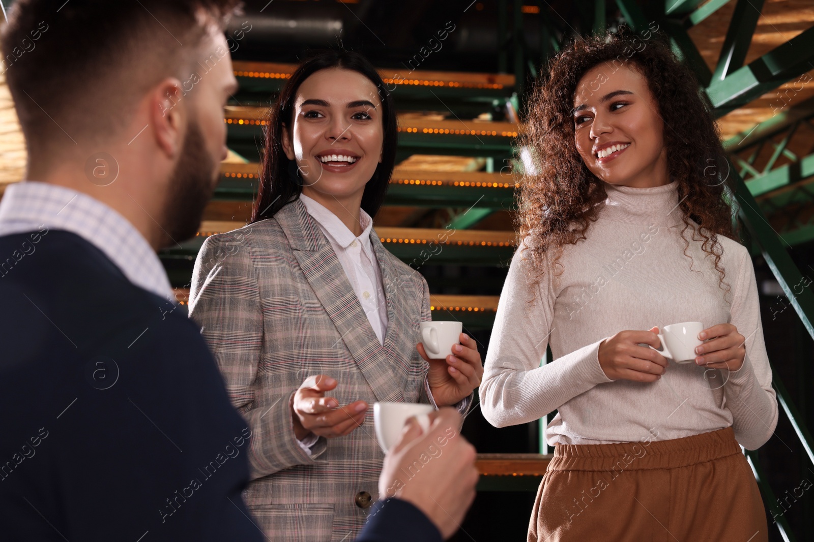 Photo of Group of coworkers talking during coffee break on stairs in office