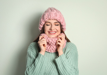 Photo of Young woman wearing warm sweater, snood and hat on light background. Winter season