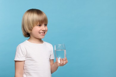 Photo of Happy little boy holding glass of fresh water on light blue background, space for text
