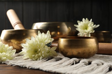 Photo of Tibetan singing bowls with beautiful flowers and mallet on wooden table