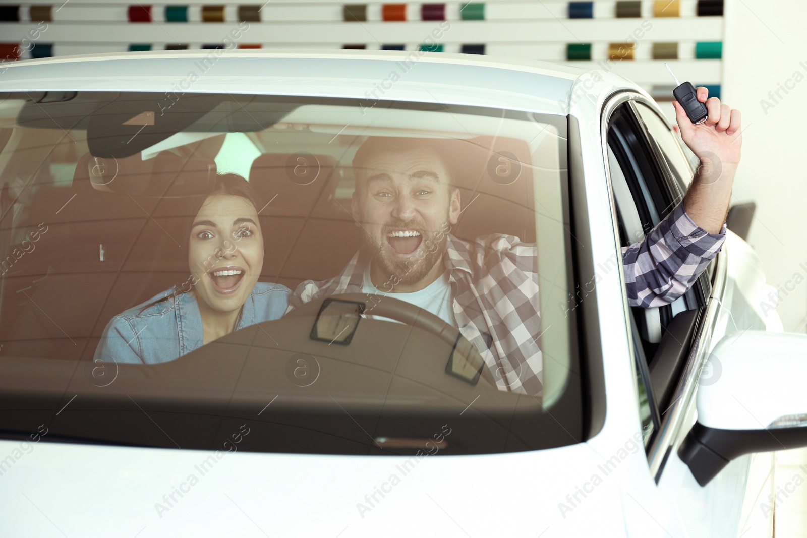 Photo of Happy couple with car key sitting in modern auto at dealership