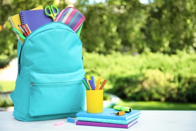 Bright backpack and school stationery on table outdoors, space for text