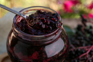 Photo of Taking tasty elderberry (Sambucus) jam with spoon from glass jar, closeup