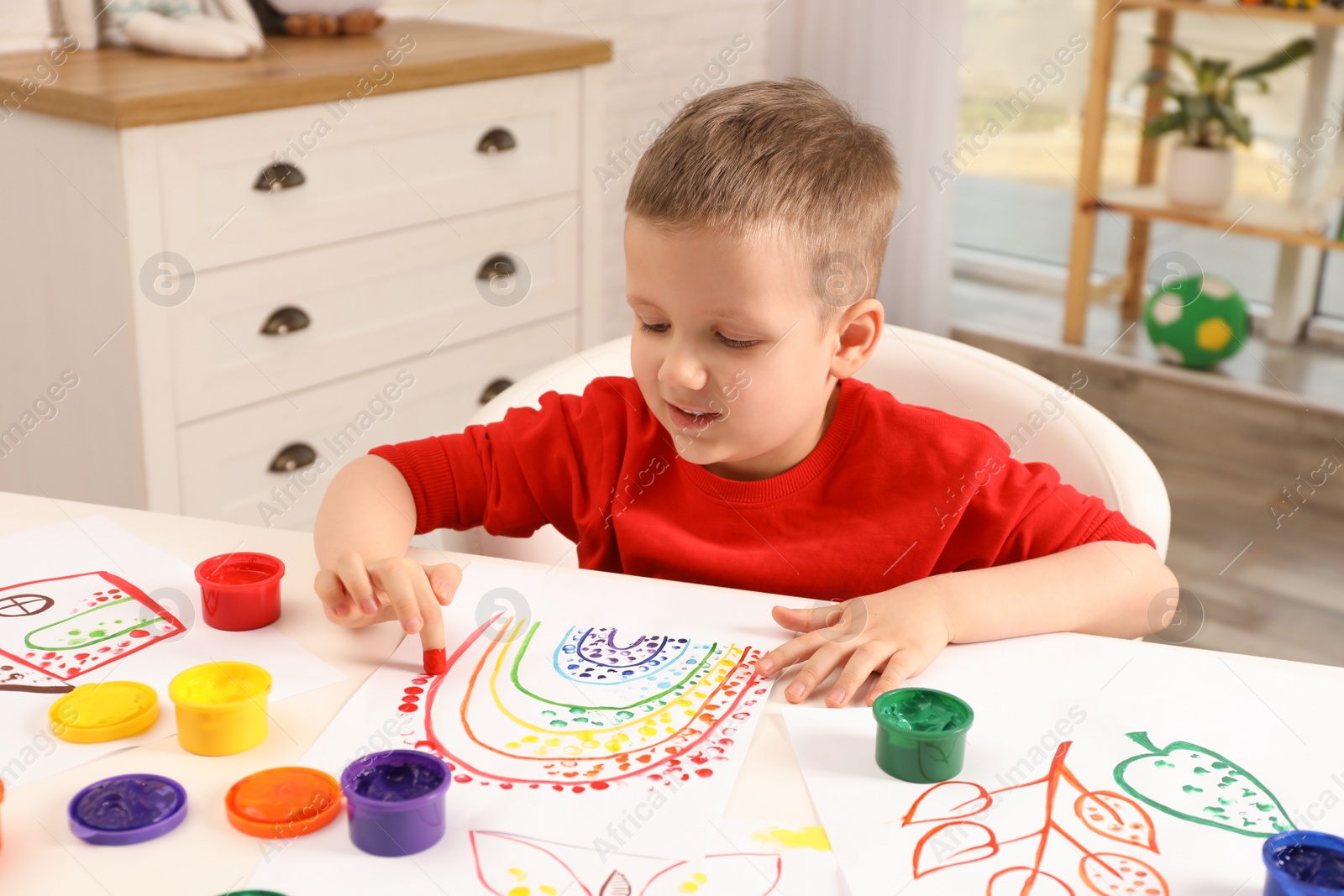 Photo of Little boy painting with finger at white table indoors