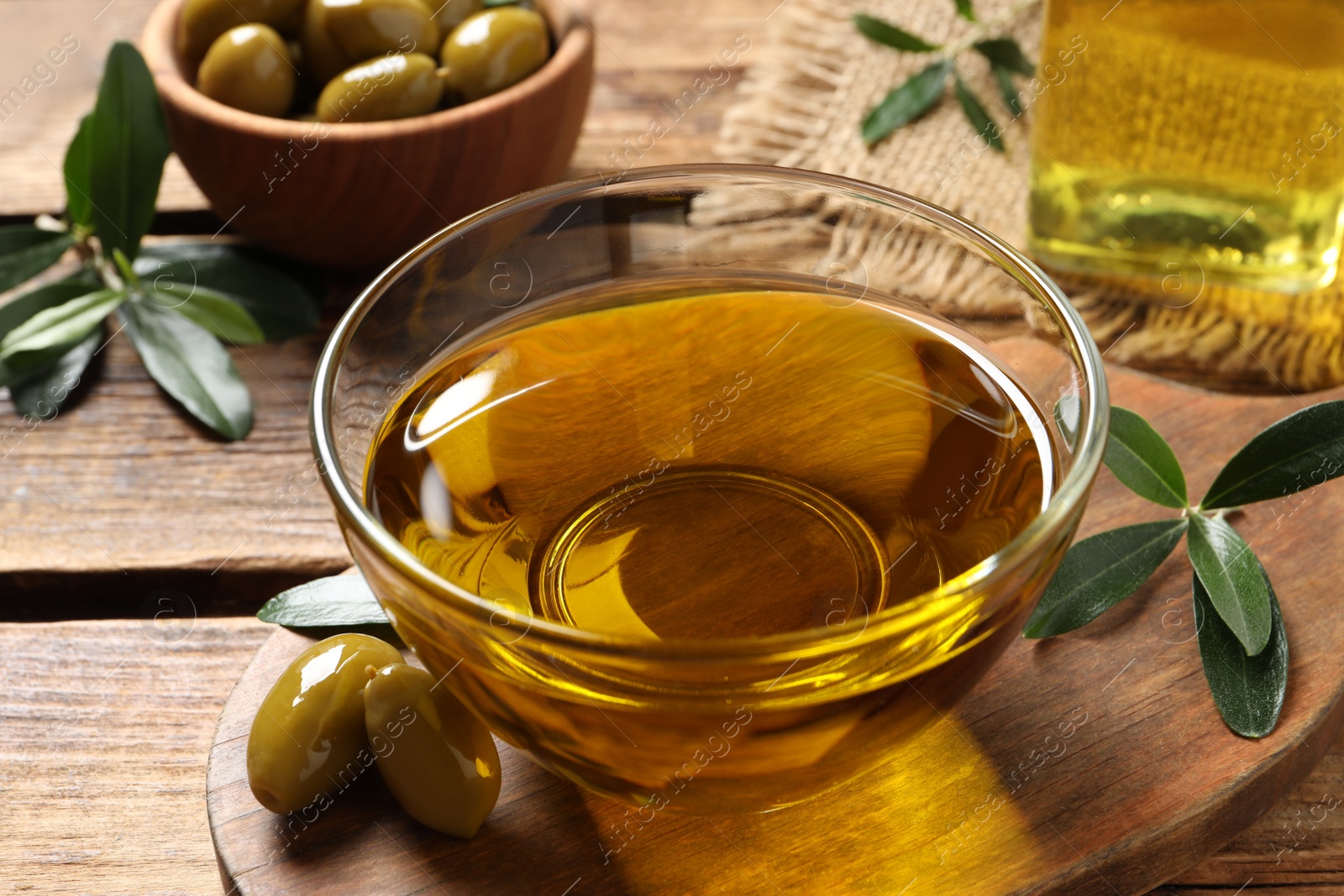 Photo of Glass bowl of oil, ripe olives and green leaves on wooden table, closeup