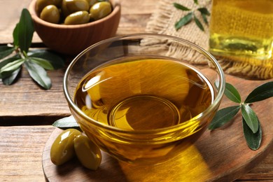 Photo of Glass bowl of oil, ripe olives and green leaves on wooden table, closeup