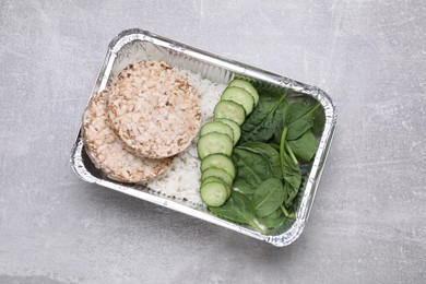 Container with rice, puffed crunchy cakes. fresh spinach and cut cucumbers on light grey table, top view
