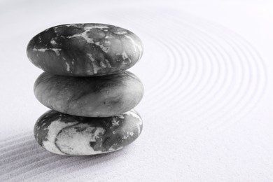 Photo of Zen garden stones on white sand with pattern, closeup. Space for text