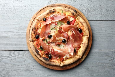 Photo of Tasty pizza with cured ham, olives and sun-dried tomato on gray wooden table, top view