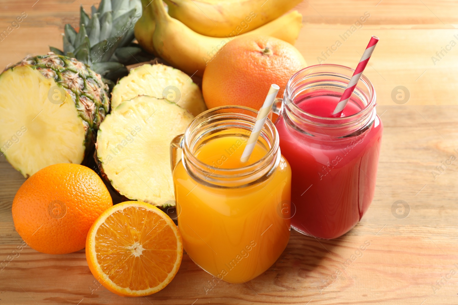 Photo of Different juices in mason jars and fresh fruits on wooden table