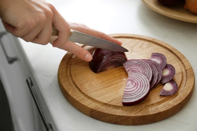 Woman cutting red onion into slices at countertop in kitchen, closeup