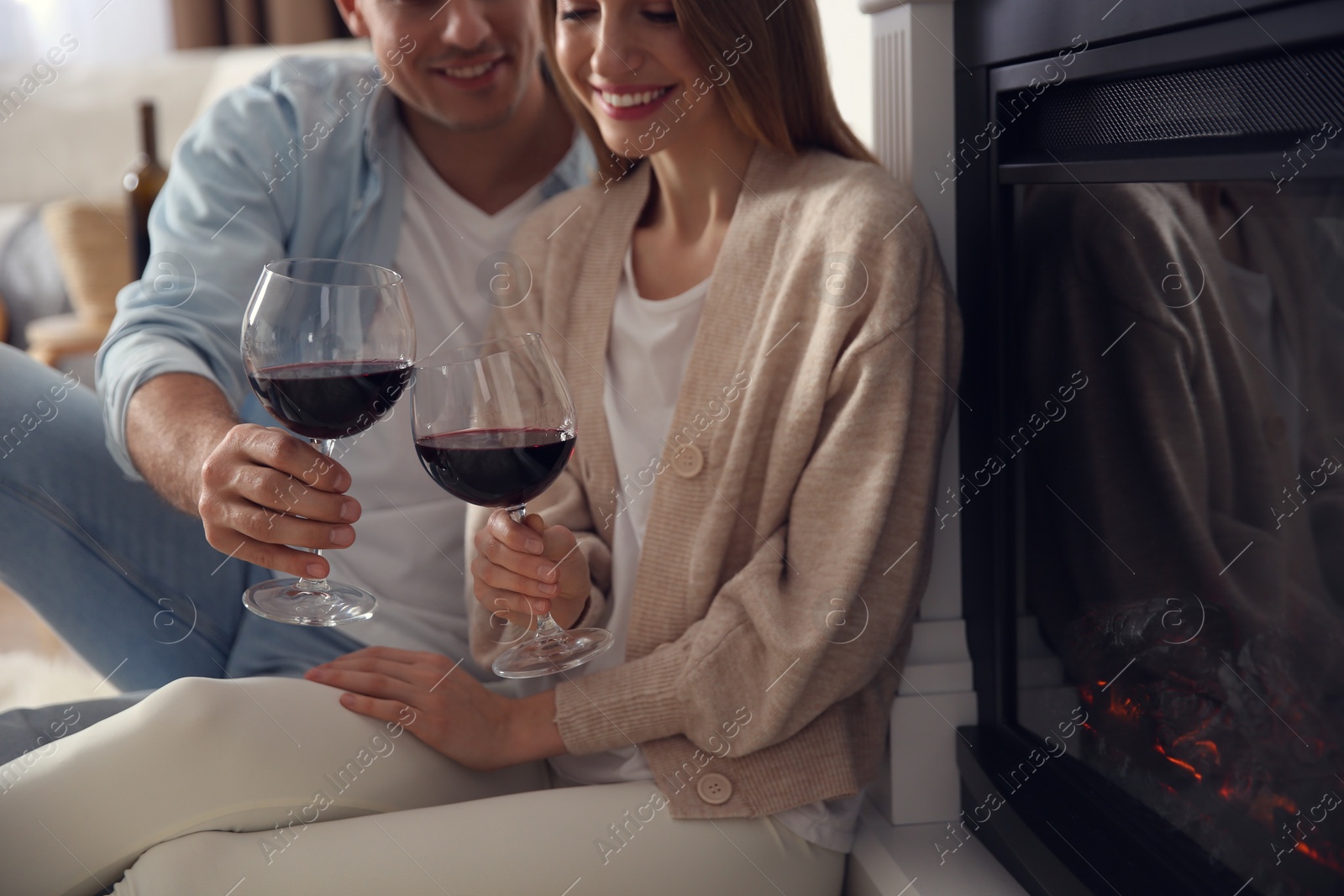 Photo of Happy couple with glasses of wine resting near fireplace at home