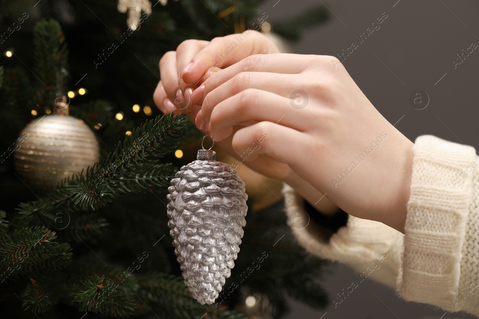 Photo of Woman decorating Christmas tree with beautiful bauble on grey background, closeup