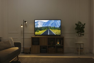 Image of Modern TV set on wooden stand in room. Scene of nature themed movie on screen