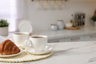 Photo of Breakfast served in kitchen. Cups of coffee and fresh croissant on white marble table. Space for text