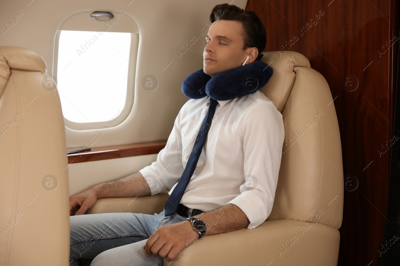 Photo of Young man with travel pillow resting while listening to music in airplane during flight