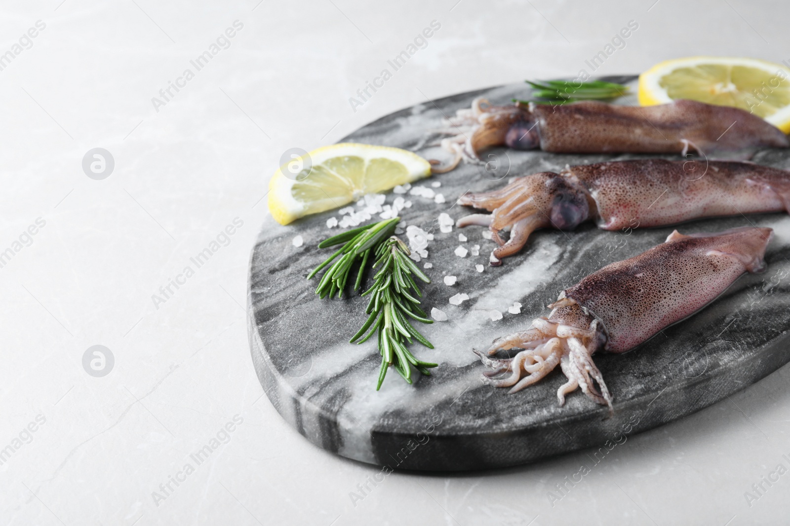 Photo of Fresh raw squids with lemon, rosemary and salt on light grey marble table. Space for text